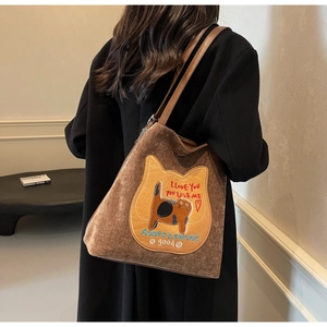 Dettaglio borsa tote in velluto marrone con toppa a gatto indossata dal modello