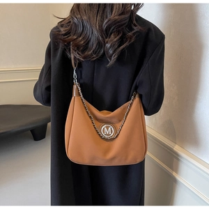 Detail of a brown leather shoulder bag featuring a metallic M logo and chain strap