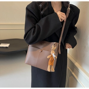 Detail of brown lychee texture leather crossbody bag with a cute plush rabbit charm