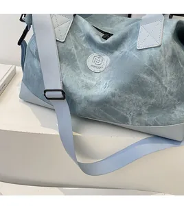 Close-up of light blue washed canvas travel bag with adjustable strap and logo detail