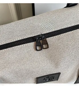 Detail of smooth double zippers and leather logo patch on beige woven travel bag