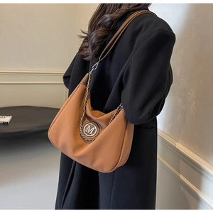 Detail of caramel leather hobo bag with silver M logo and decorative metal chain