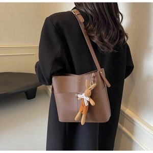 Detail of a brown leather bucket bag with a rabbit plush charm on a black coat background