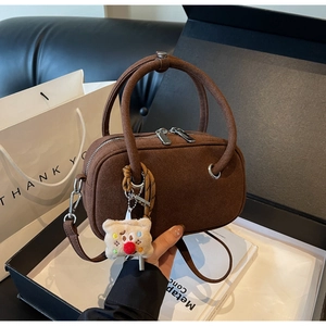 Détail du sac bandoulière en daim marron avec poignées rondes et pendentif en peluche