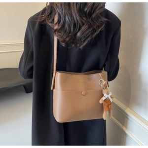 Brown bucket bag in lychee texture with a plush bunny charm shown on model back view