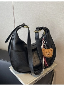 Fashionable black hobo crossbody bag with bear pendant and adjustable strap on books