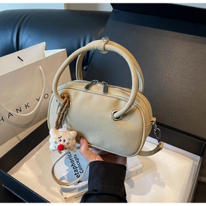 Détail d'un sac Boston en daim beige avec zips argentés et charm peluche sur l'anse