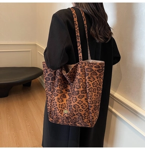 Detailed view of leopard print tote bag with gold metal logo worn with black coat