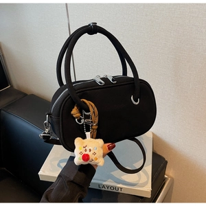 Détail du sac à main noir avec poignée ronde et pendentif en peluche sur des livres