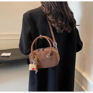 Détail d'un sac à main en daim marron avec boucles argentées et breloque peluche sur mannequin