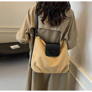 Close-up of yellow suede tote bag with black leather flap and decorative round buckle