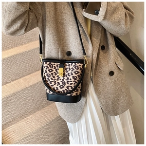 Leopard print bucket bag with gold hardware worn over a brown wool blazer and white skirt