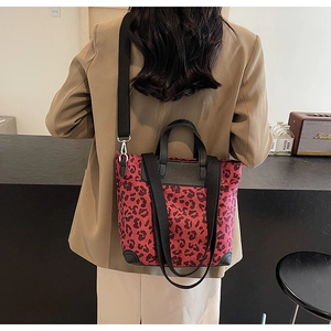 Detail shot of a red leopard print tote bag with black leather straps on a model