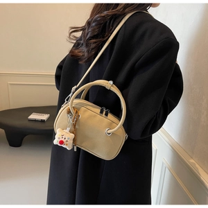 Détail d'un sac Boston en daim beige avec breloque ours porté sur un manteau noir