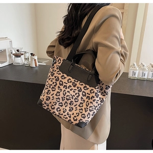 Leopard print tote bag with black wide strap shown on a model in a cafe setting