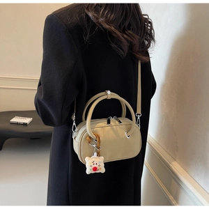 Détail d'un sac bandoulière beige avec pendentif en peluche et double poignées sur blazer