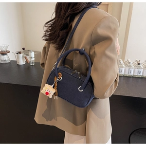 Détail du sac bandoulière bleu marine avec poignée ronde et breloque en peluche sur modèle