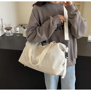 Action shot of beige large travel bag with wide shoulder strap used as a crossbody bag