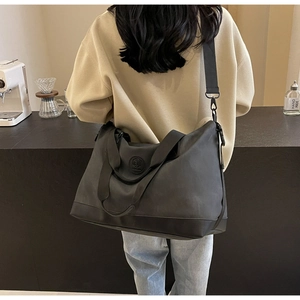 Detail of black large capacity travel tote bag with logo and adjustable strap worn by model