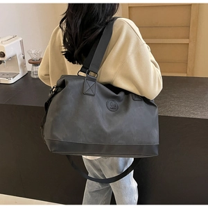 Black large travel duffel bag with shoulder strap worn by a model in a cafe setting