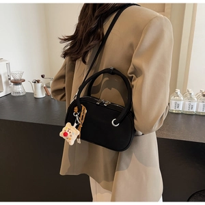 Détail du sac à main noir mat avec double poignée et breloque en forme d'ours mignon