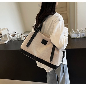 Détail du cabas en toile montrant la texture beige et les bordures en cuir noir chic