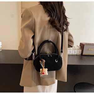 Détail du sac bandoulière noir avec fermetures éclair argentées et breloque ours en peluche