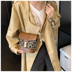 Detail view of a leopard print crossbody bucket bag worn with a khaki trench coat