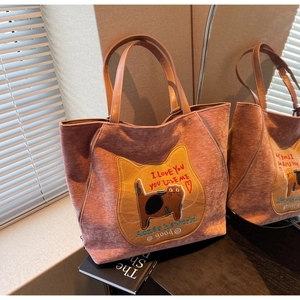 Dettaglio della borsa tote in velluto rosa con patch di gatto e manici in pelle marrone