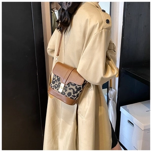 Detail of leopard print patchwork crossbody bucket bag with gold buckle on trench coat