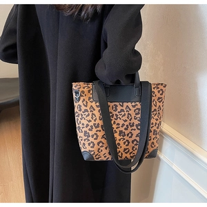 Leopard print tote bag with black shoulder strap worn over a black winter coat