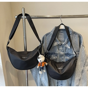 Détail de sacs à bandoulière demi-lune en nylon noir avec logo blanc et breloque taureau