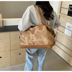 Brown canvas travel bag with leather trim carried by a woman in a cozy room