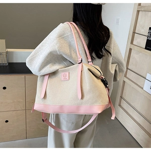 Détail du grand sac de voyage en toile beige avec finitions roses porté par un mannequin