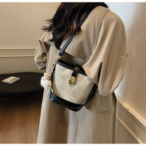 Detail van beige en zwarte emmertas met gouden sluiting en pluche hanger op trenchcoat