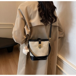 Model draagt een tweekleurige canvas emmer-tas met zwart lederen bies en pluche hanger