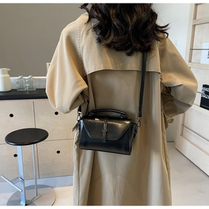 Detailed view of women's black glossy leather handbag with refined metal buckle and top handle
