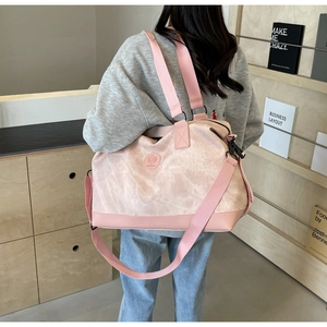 Woman carrying large pink travel bag with shoulder strap in a modern indoor setting