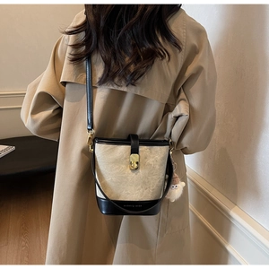 Detail van een tweekleurige emmertas met gouden slot en pluche hanger op een trenchcoat