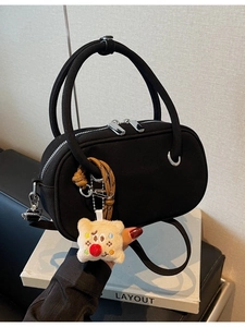 Sac bandoulière noir vintage avec poignée ronde et breloque peluche sur un livre