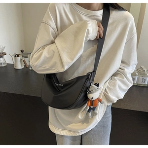 Détail du sac bandoulière noir en demi-lune avec logo blanc et breloque loup en peluche