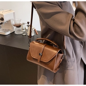 Brown vintage leather crossbody bag featuring a classic metal buckle closure on model