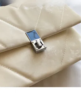 Close-up of silver metal clasp and quilted stitching on beige faux leather bag