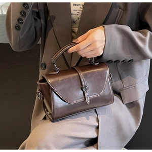 Detail of dark brown leather handbag with round metal clasp and flap on grey blazer