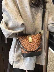 Fashionable leopard print bucket bag with gold hardware and black leather strap worn by a model
