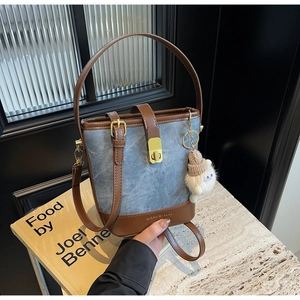 Detail van de bucket bag van blauwe denim en bruin leer met een witte pluche hanger