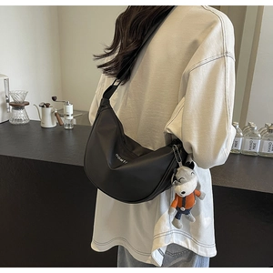 Détail du sac bandoulière demi-lune noir avec logo OOMTI et breloque loup en peluche