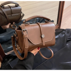 Detail view of brown leather crossbody bag with silver buckle and cylindrical handle