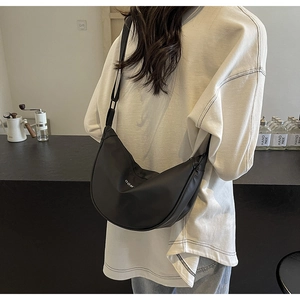 Vue détaillée du sac à bandoulière noir mat en forme de croissant dans un café chic