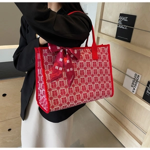 Close-up of a red knitted tote bag featuring white Xi characters and decorative silk scarf